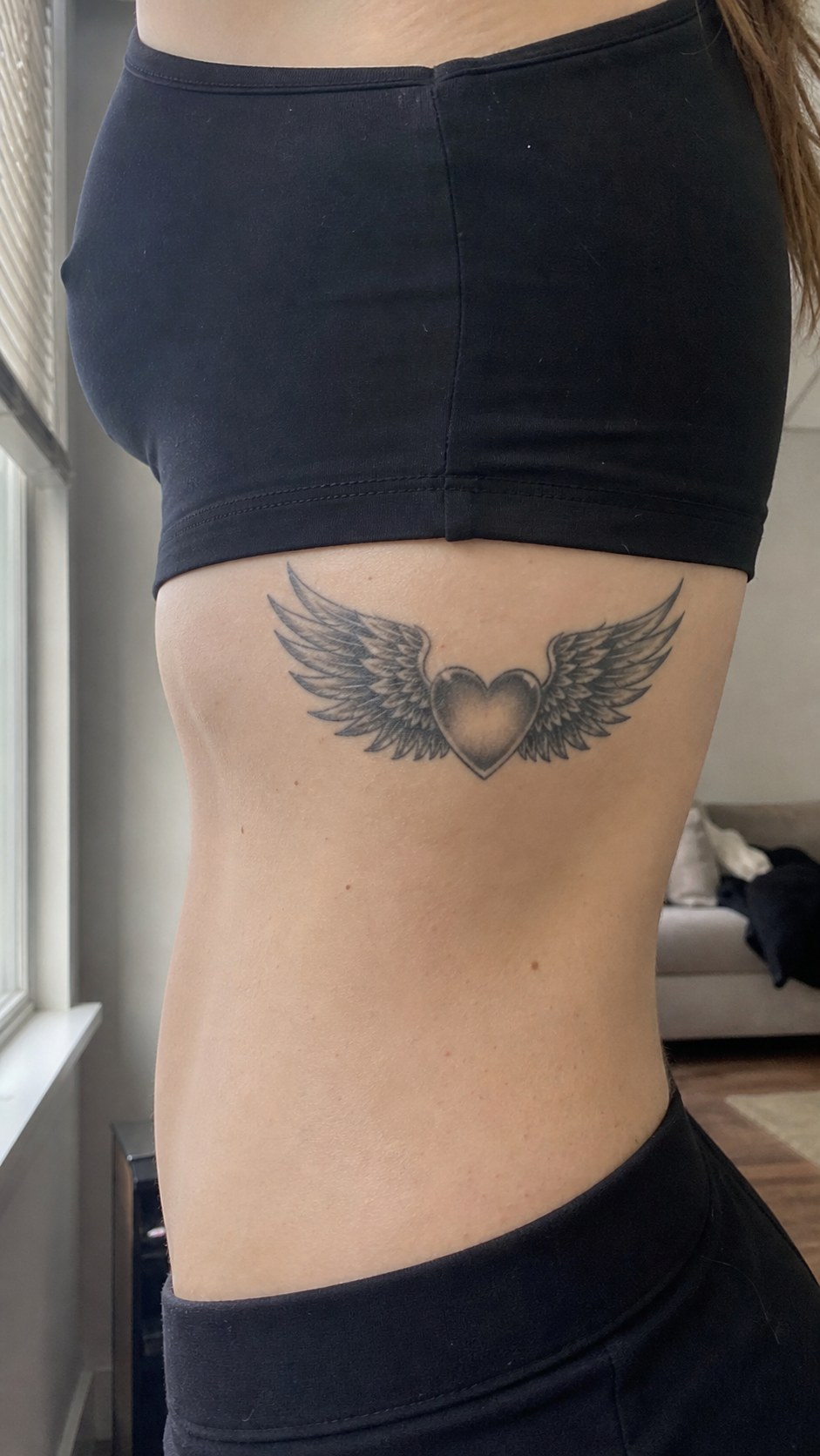 Healed winged heart tattoo on a adult woman's behind the ear, photographed in a natural straight-on close view, a touch off-center — study 1