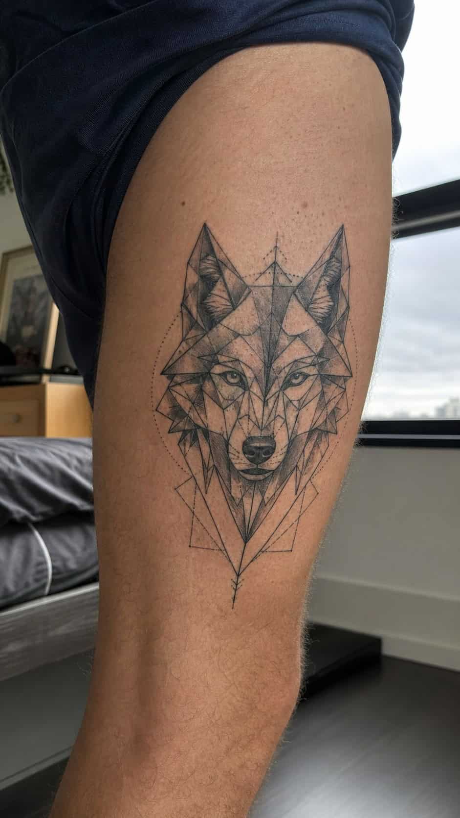 Feeling Bold? Try These 25 Killer Thigh Tattoo Ideas for Men 7 Healed geometric wolf head tattoo on a adult man's outer thigh, photographed in a natural casual close three-quarter view — study 2