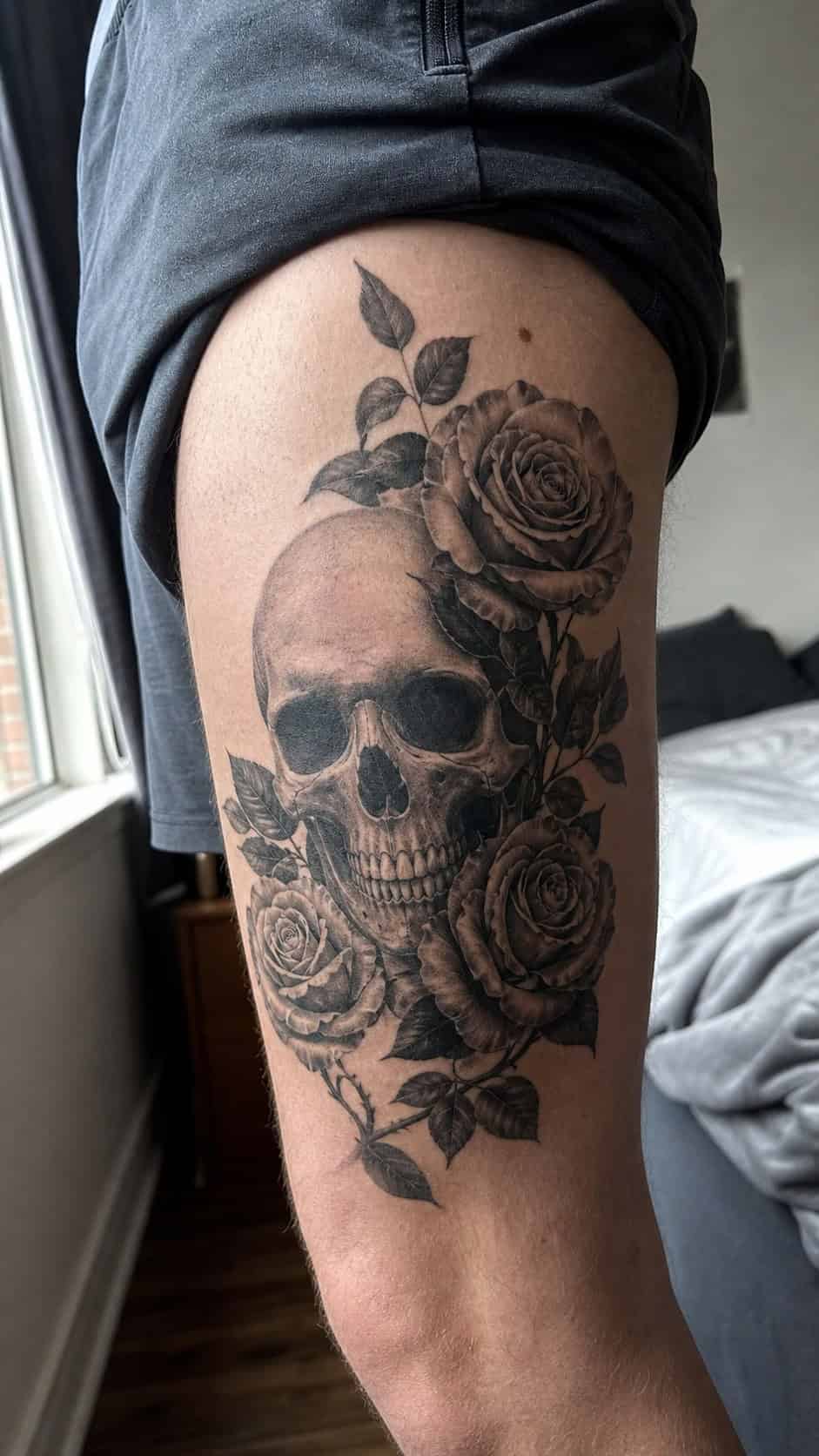 Feeling Bold? Try These 25 Killer Thigh Tattoo Ideas for Men 16 Healed realistic skull and roses tattoo on a adult man's outer thigh, photographed in a natural slightly elevated close view — study 1