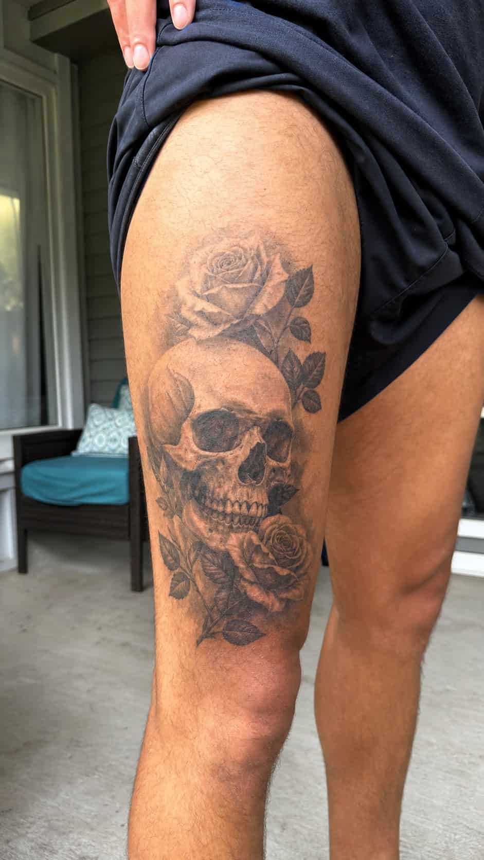 Feeling Bold? Try These 25 Killer Thigh Tattoo Ideas for Men 17 Healed realistic skull and roses tattoo on a adult man's outer thigh, photographed in a natural waist-height candid close-up — study 2