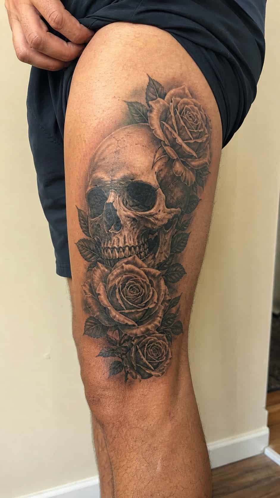 Feeling Bold? Try These 25 Killer Thigh Tattoo Ideas for Men 18 Healed realistic skull and roses tattoo on a adult man's outer thigh, photographed in a natural relaxed documentary crop — study 3
