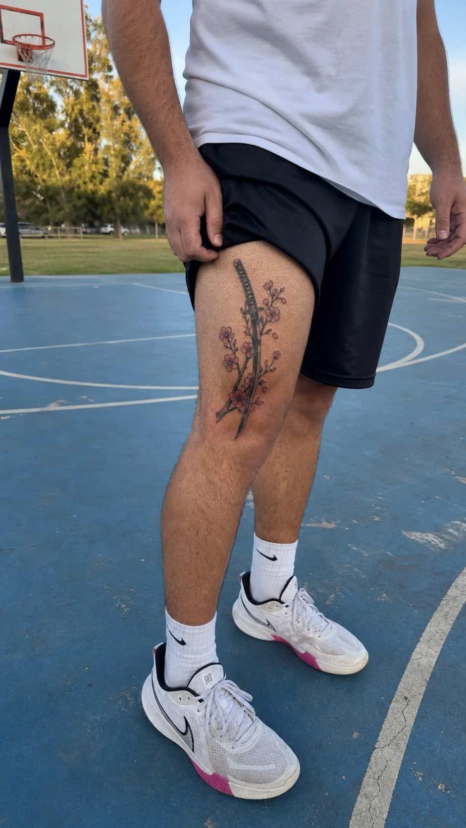 Feeling Bold? Try These 25 Killer Thigh Tattoo Ideas for Men 41 Healed samurai sword and cherry blossoms tattoo on a adult man's outer thigh, photographed in a natural waist-height candid close-up — study 1