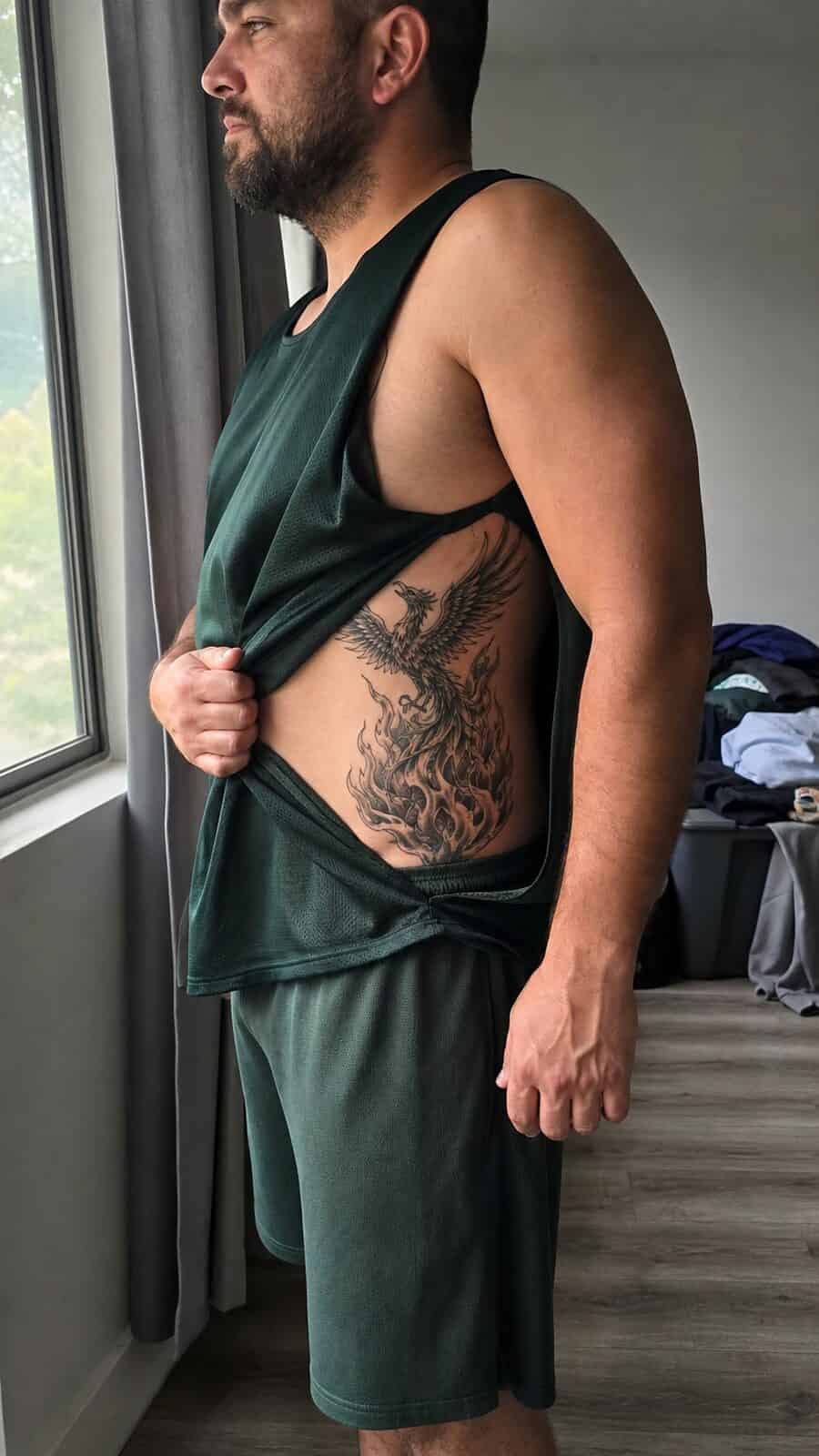 25 Rib Tattoos for Men Worth Considering 14 Healed phoenix rising tattoo on a adult man's side ribs, photographed in a natural casual close three-quarter view — study 2