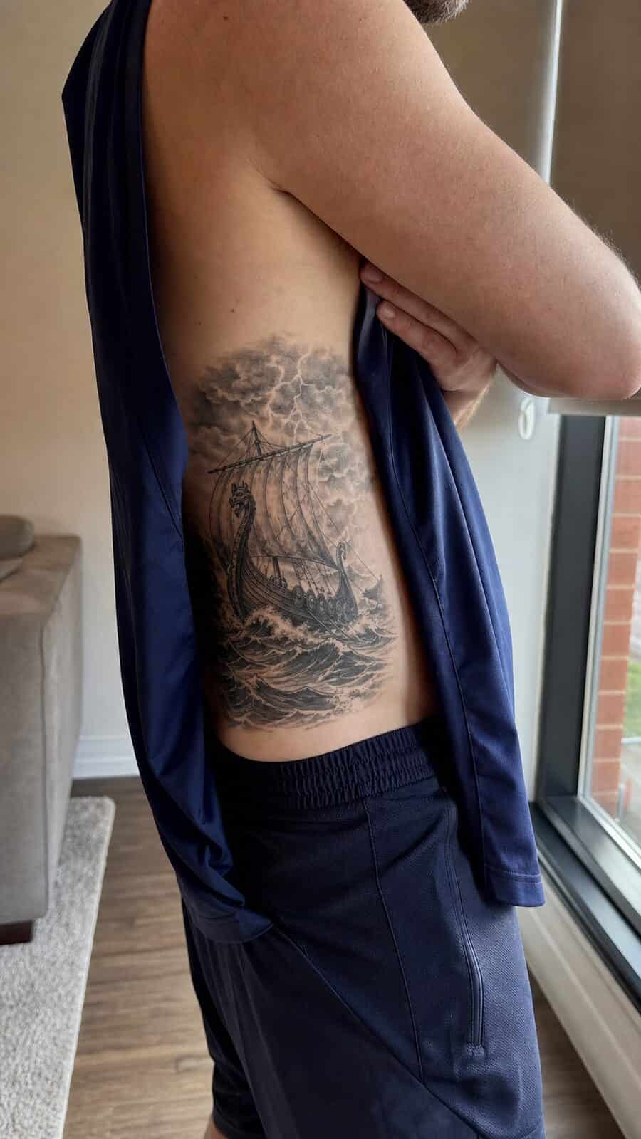 25 Rib Tattoos for Men Worth Considering 23 Healed viking ship tattoo on a adult man's side ribs, photographed in a natural gentle side angle that clearly shows how the ink wraps — study 1