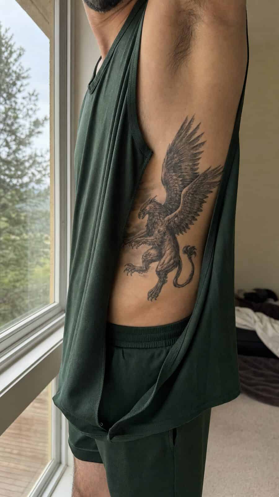 25 Rib Tattoos for Men Worth Considering 29 Healed mythical griffin tattoo on a adult man's side ribs, photographed in a natural waist-height candid close-up — study 3