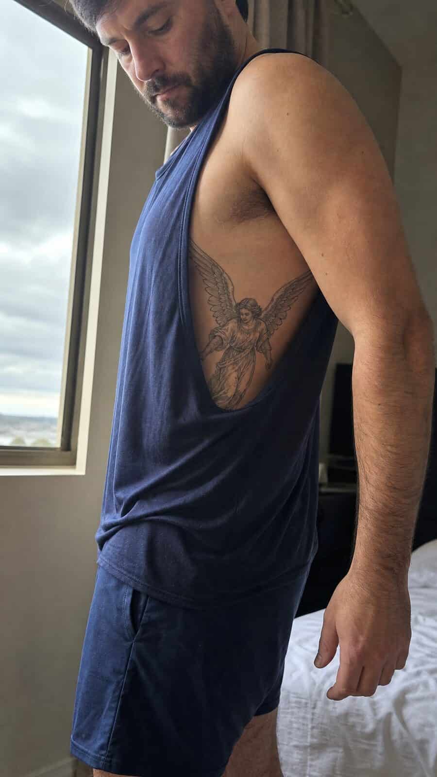 25 Rib Tattoos for Men Worth Considering 37 Healed guardian angel tattoo on a adult man's side ribs, photographed in a natural slightly elevated close view — study 2