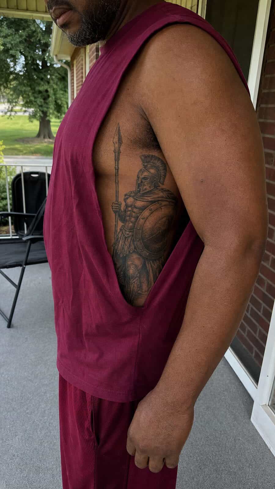 25 Rib Tattoos for Men Worth Considering 40 Healed warrior spartan tattoo on a adult man's side ribs, photographed in a natural casual close three-quarter view — study 1