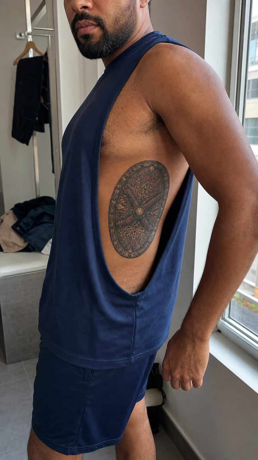 25 Rib Tattoos for Men Worth Considering 48 Healed warrior’s shield tattoo on a adult man's side ribs, photographed in a natural gentle side angle that clearly shows how the ink — study 2