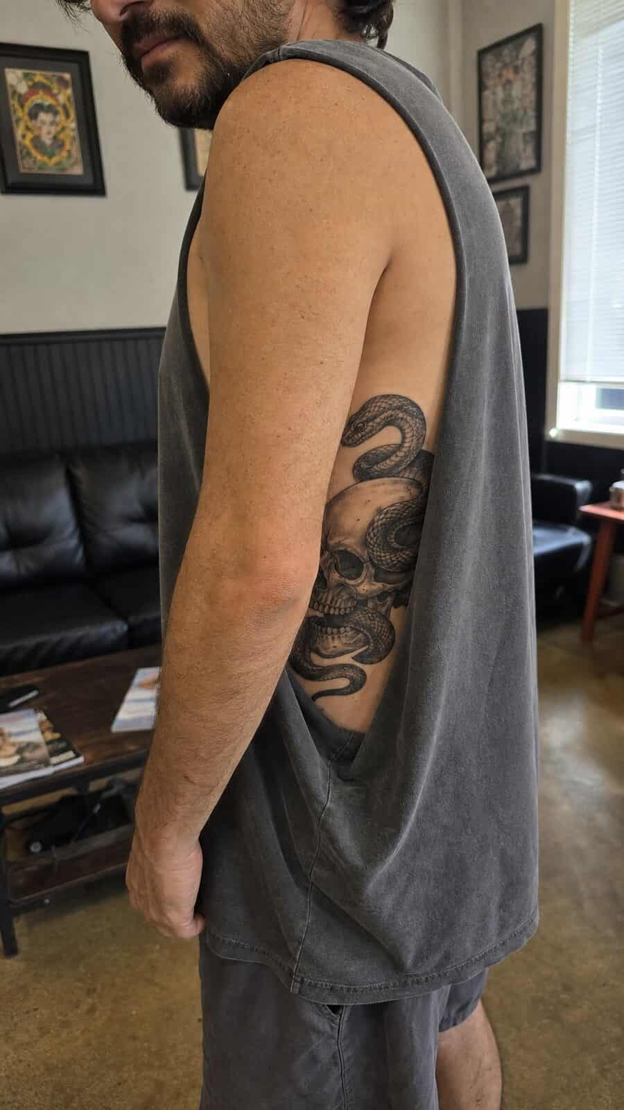 25 Rib Tattoos for Men Worth Considering 49 Healed serpent and skull tattoo on a adult man's side ribs, photographed in a natural waist-height candid close-up — study 1