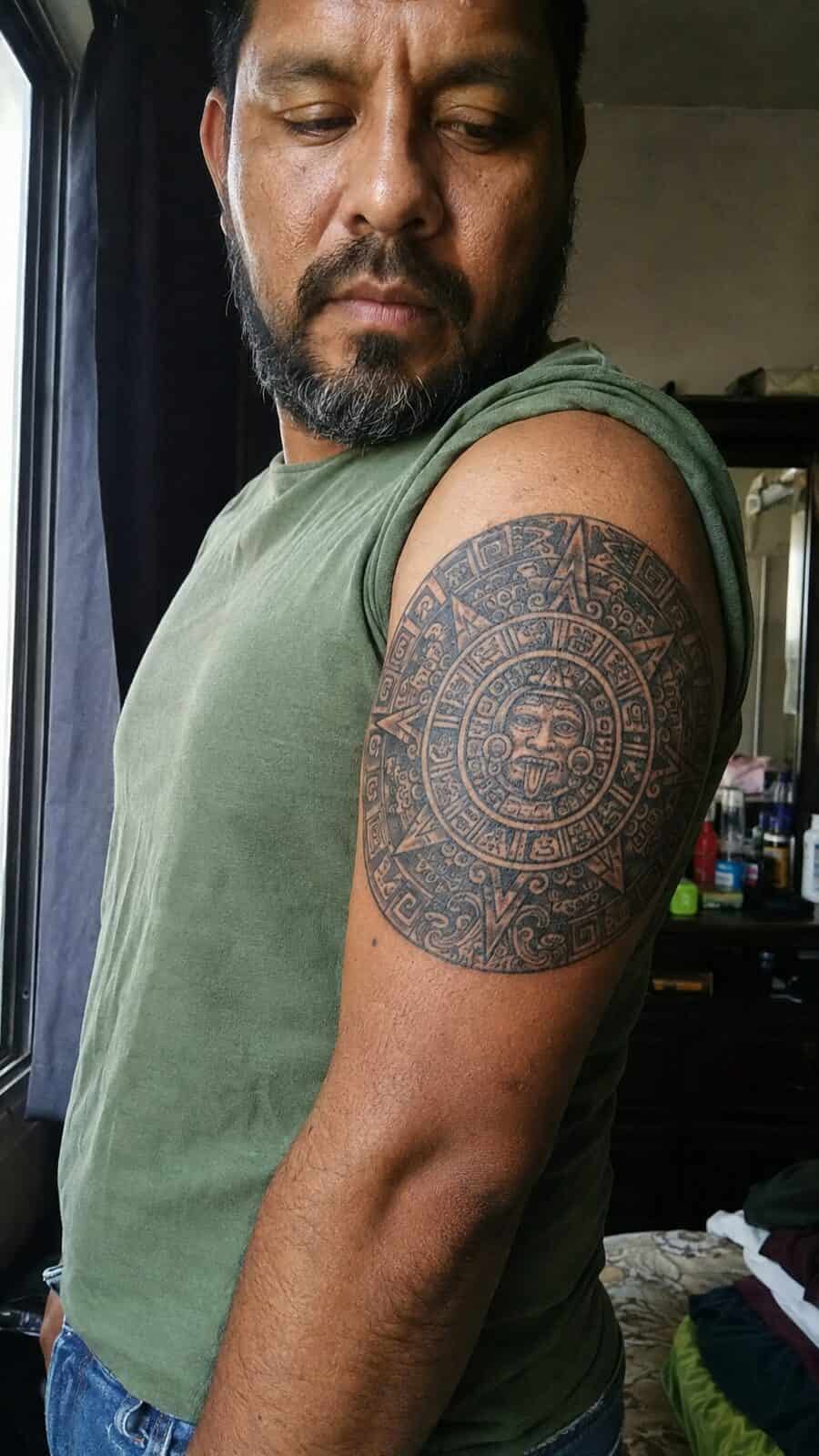 Unlock Your Next Ink: 25 Epic Upper Arm Tattoo Ideas for Men 52 Healed aztec sun tattoo on a adult man's outer upper arm, photographed in a natural waist-height candid close-up — study 1