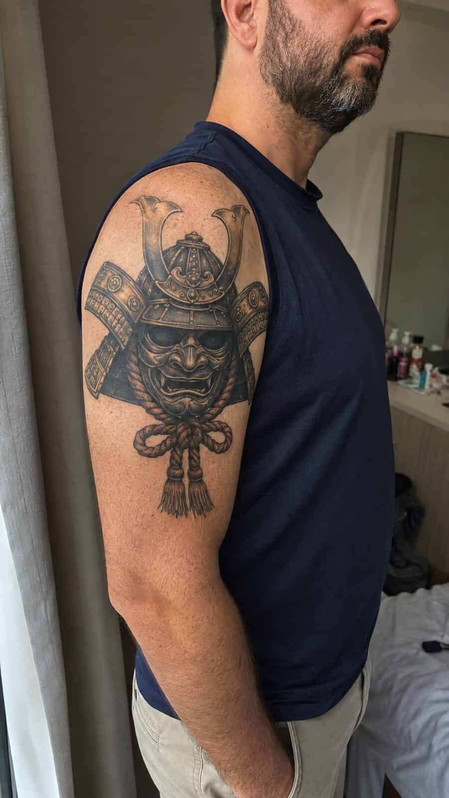 Unlock Your Next Ink: 25 Epic Upper Arm Tattoo Ideas for Men 63 Healed samurai mask tattoo on a adult man's outer upper arm, photographed in a natural casual close three-quarter view — study 3