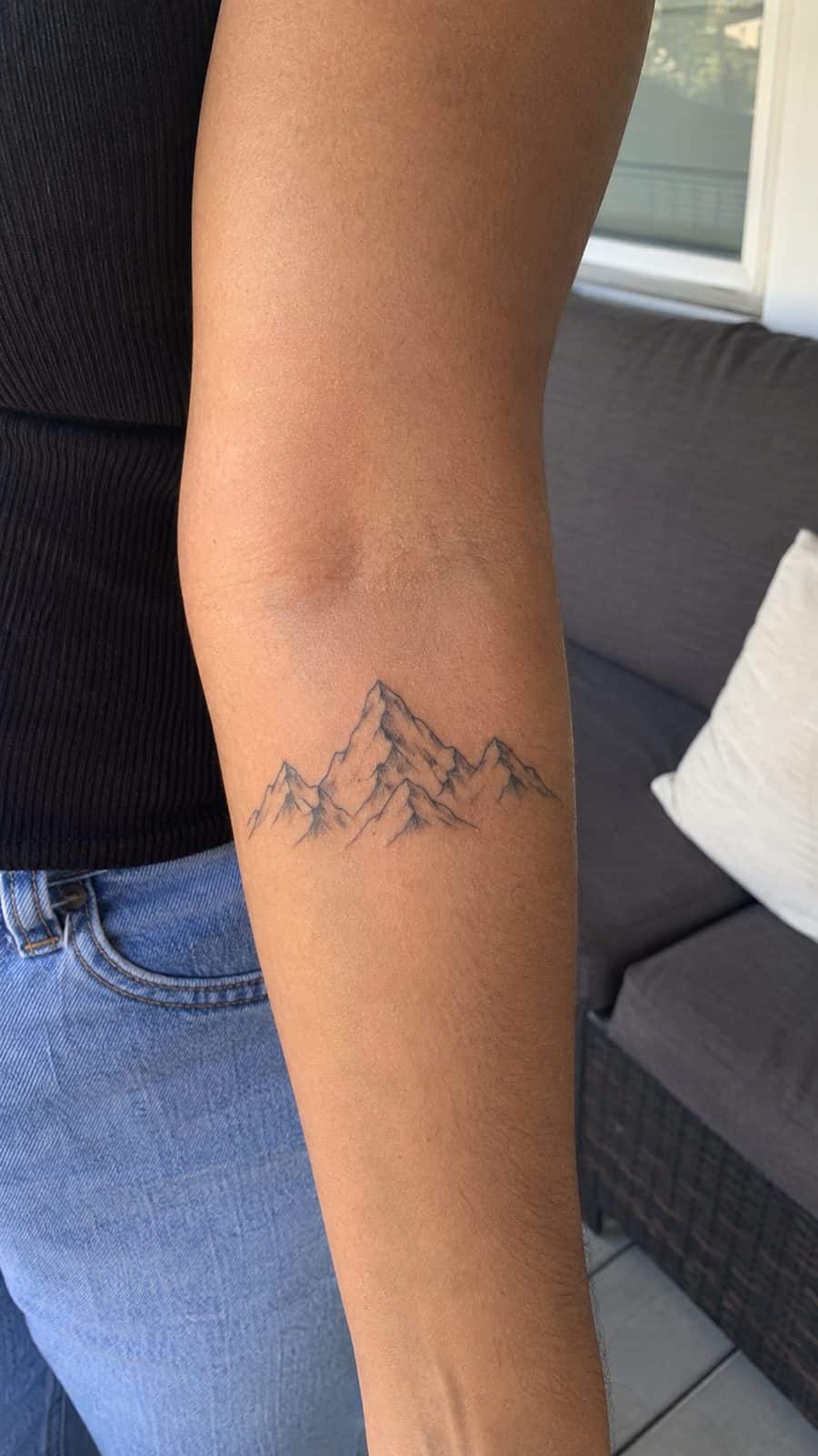 35 Forearm Tattoos for Women Worth Considering 12 Healed minimalist mountains tattoo on a adult woman's inner forearm, photographed in a natural slightly elevated close view — study 2