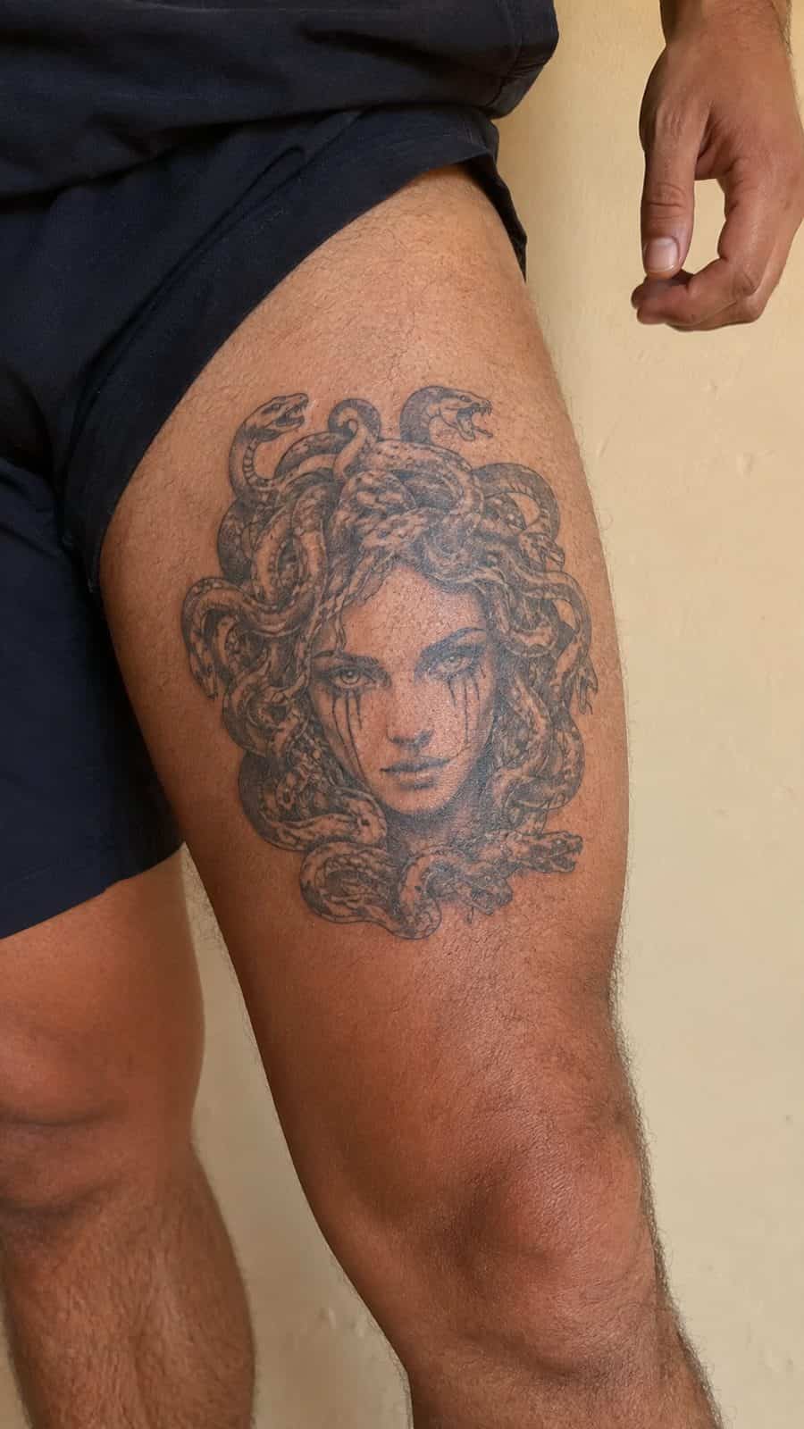 Modern Spartan: 18 Greek Tattoo Ideas Every Man Should Consider 11 Healed medusa's gaze tattoo on a adult man's outer thigh, photographed in a natural casual close three-quarter view — study 2