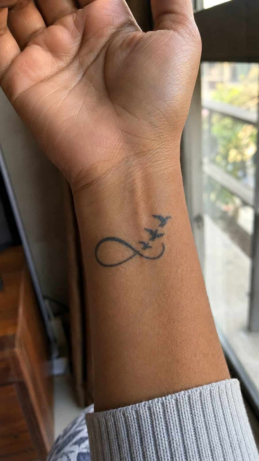 Wrist Tattoos Women Are Raving About: Discover the 28 Most Gorgeous Designs 6 Healed infinity symbol with birds tattoo on a adult woman's inner wrist, photographed in a natural casual close three-quarter view — study 1