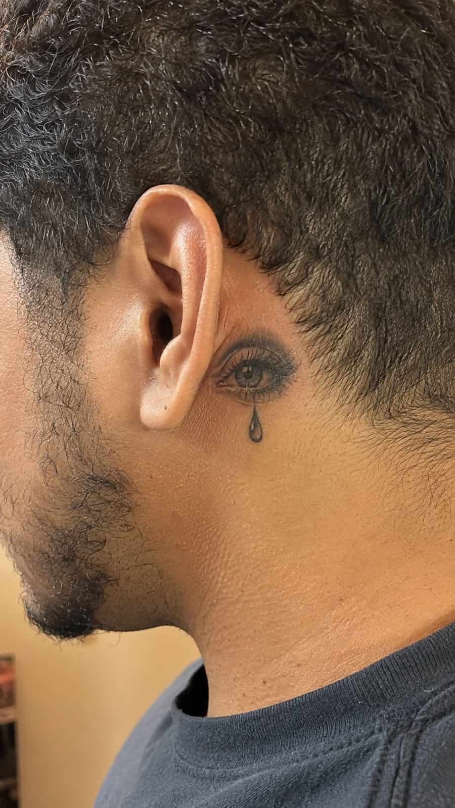 Healed tearful eye tattoo tattoo on a adult person's behind the ear, photographed in a natural straight-on close view, a touch — study 2