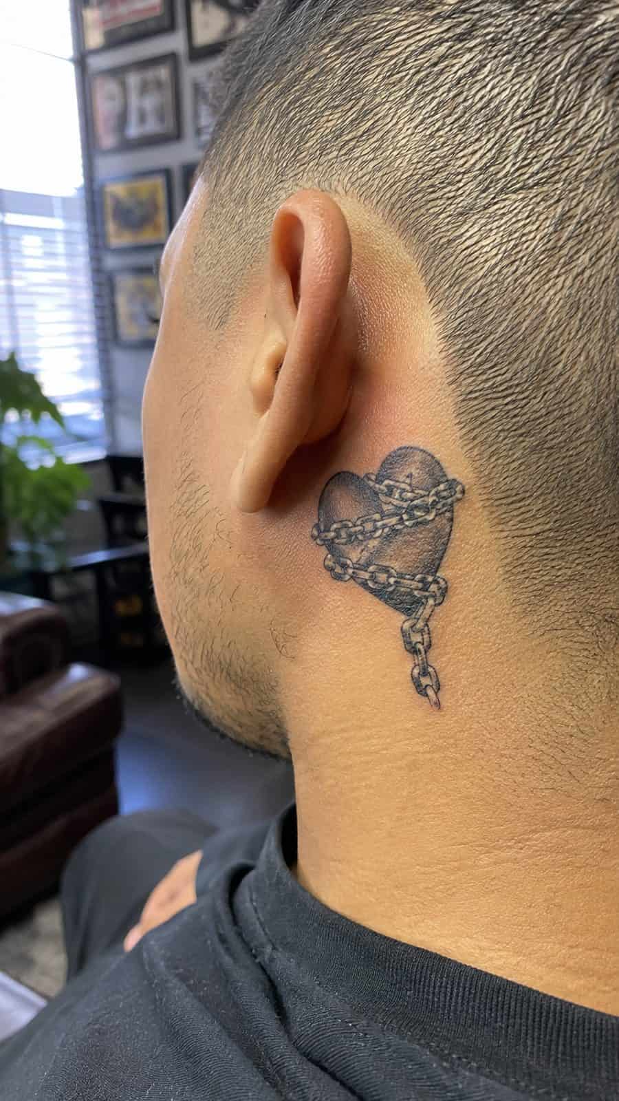 Healed heart in chains tattoo on a adult person's behind the ear, photographed in a natural waist-height candid close-up — study 1