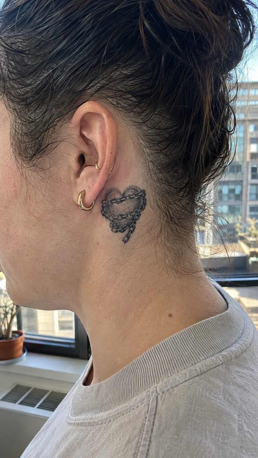 Healed heart in chains tattoo on a adult person's behind the ear, photographed in a natural relaxed documentary crop — study 2