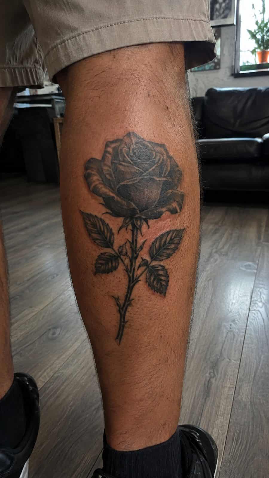 Healed black rose in bloom tattoo on a adult person's outer calf, photographed in a natural straight-on close view, a touch off-center — study 1