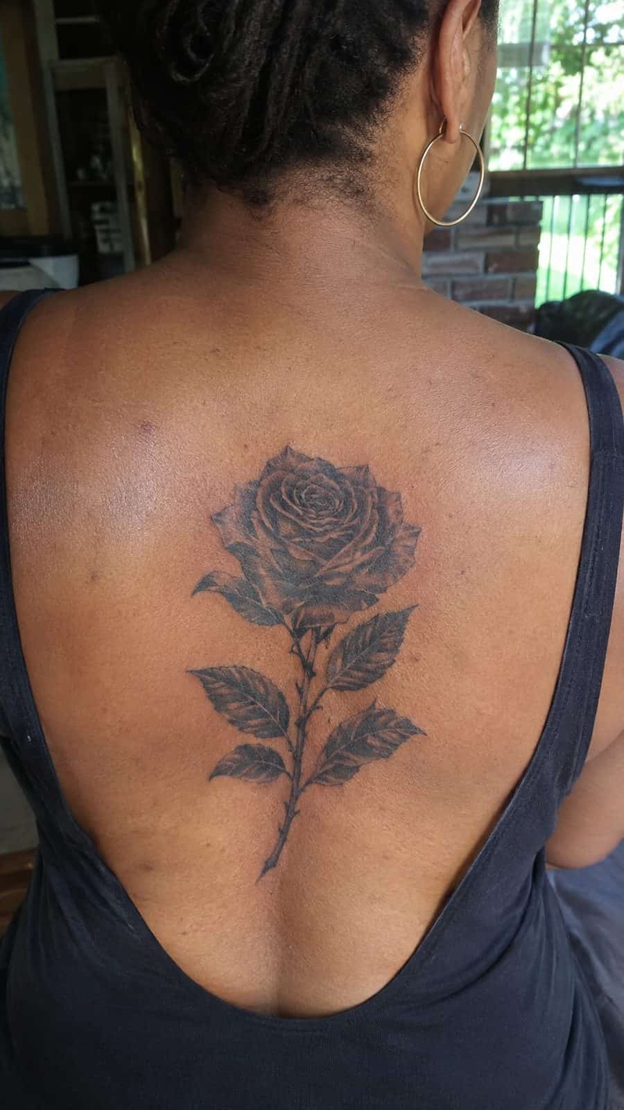 Healed black rose in bloom tattoo on a adult person's upper back, photographed in a natural slightly elevated close view — study 3