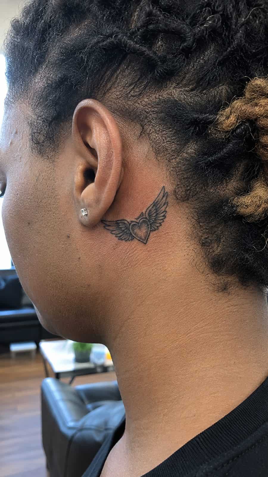 Healed winged heart tattoo on a adult person's behind the ear, photographed in a natural straight-on close view, a touch off-center — study 2
