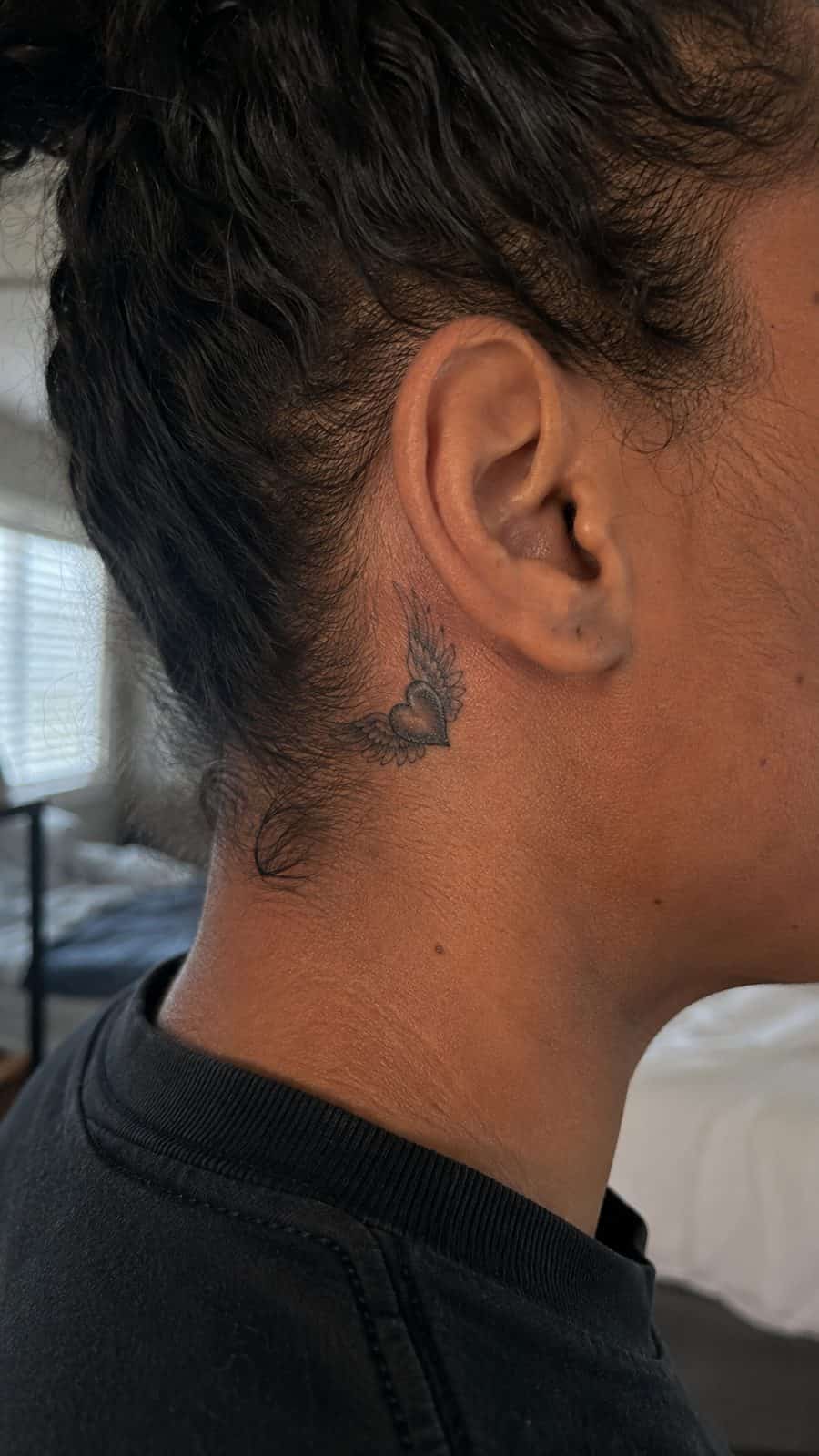 Healed winged heart tattoo on a adult person's behind the ear, photographed in a natural gentle side angle that clearly shows how the — study 3