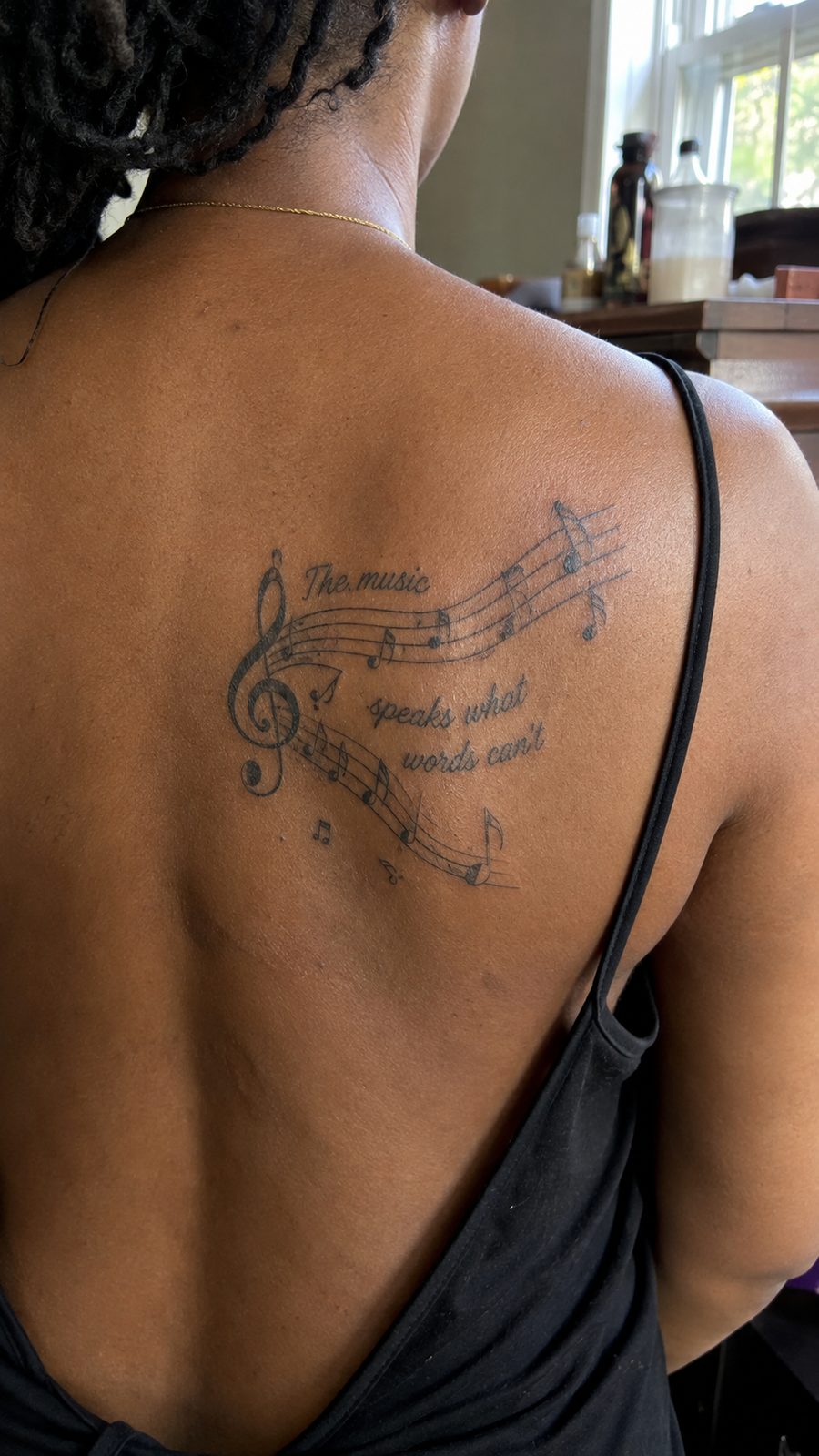 Healed music note and lyrics tattoo on a adult person's upper back, photographed in a natural slightly elevated close view — study 2