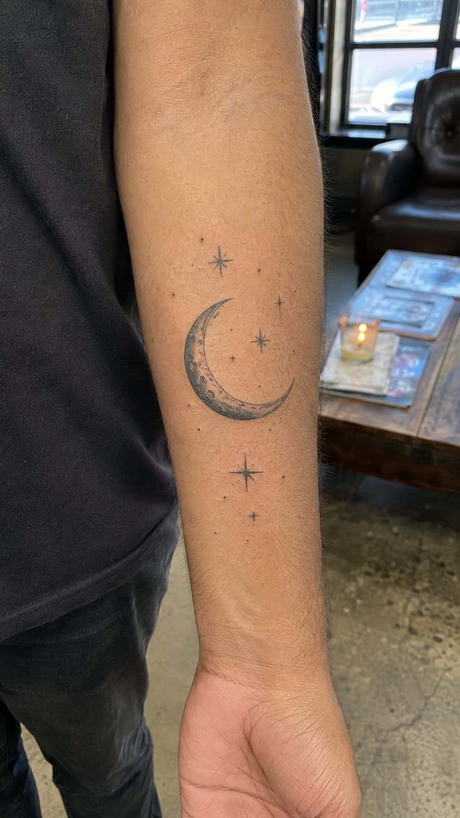 Healed crescent moon and stars tattoo on a adult person's inner forearm, photographed in a natural slightly elevated close view — study 2