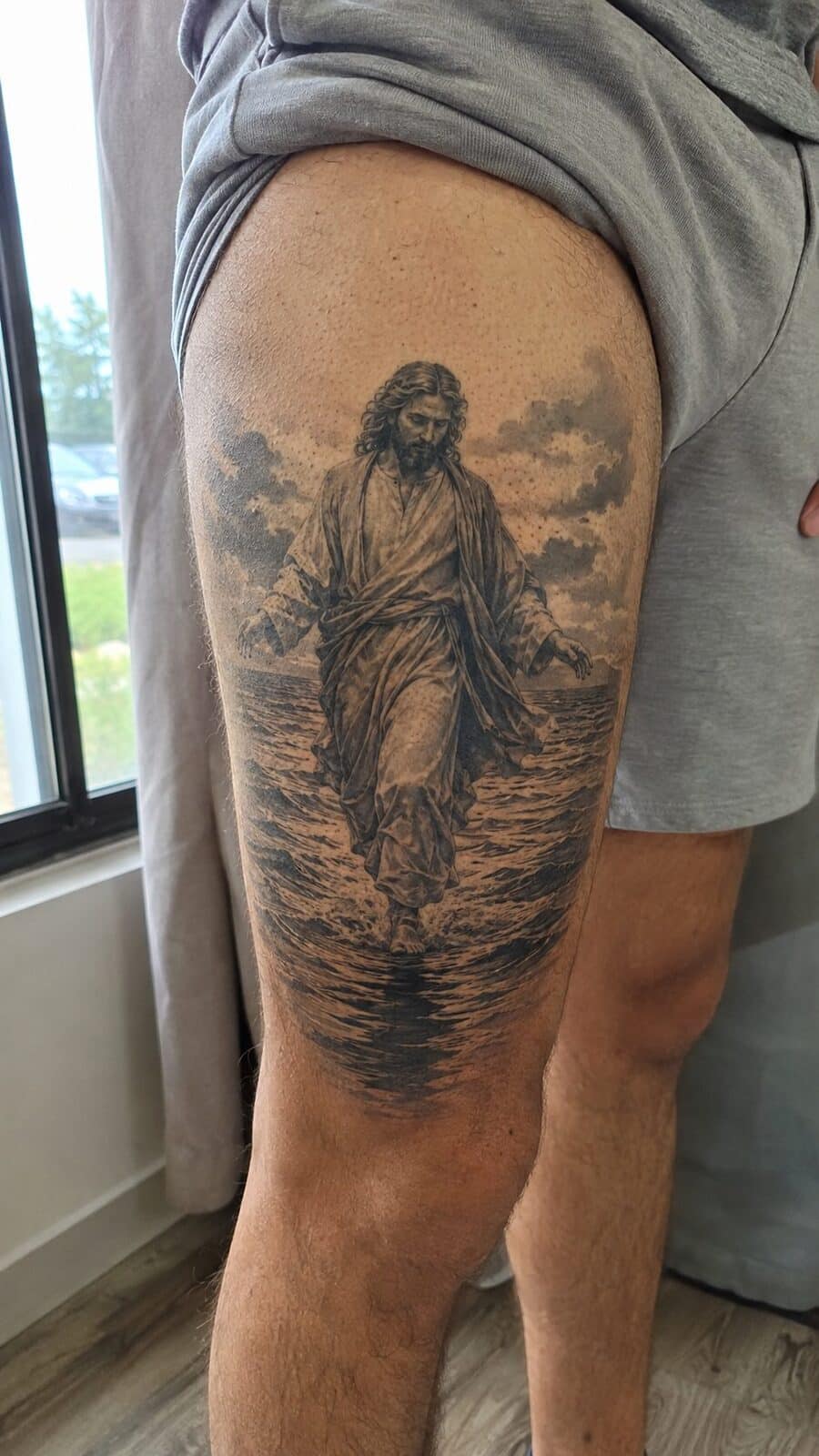 Exploring 18 Profound Jesus Tattoo Ideas for the Modern Man 7 Healed jesus walking on water tattoo on a adult man's outer thigh, photographed in a natural waist-height candid close-up — study 2