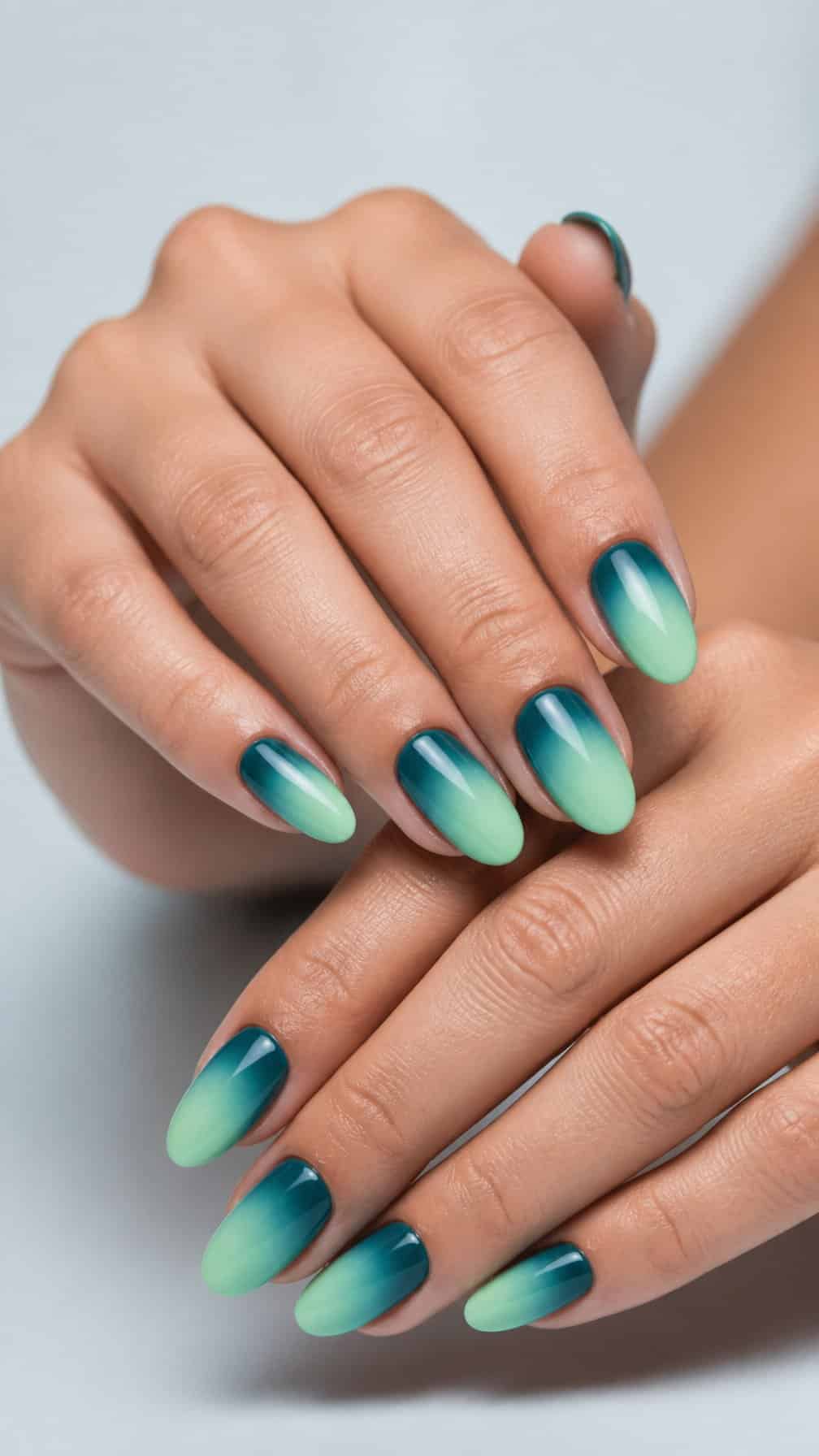 A close-up of hands with smooth teal-to-mint ombre almond-shaped manicured nails.