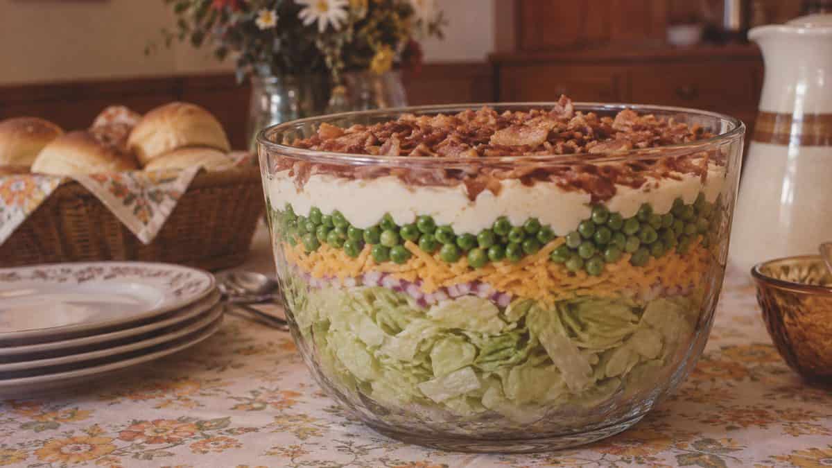 18 Church Potluck Recipes That Nobody Makes Anymore 3 Real seven-layer salad showing distinct layers of lettuce, peas, mayo, and bacon.