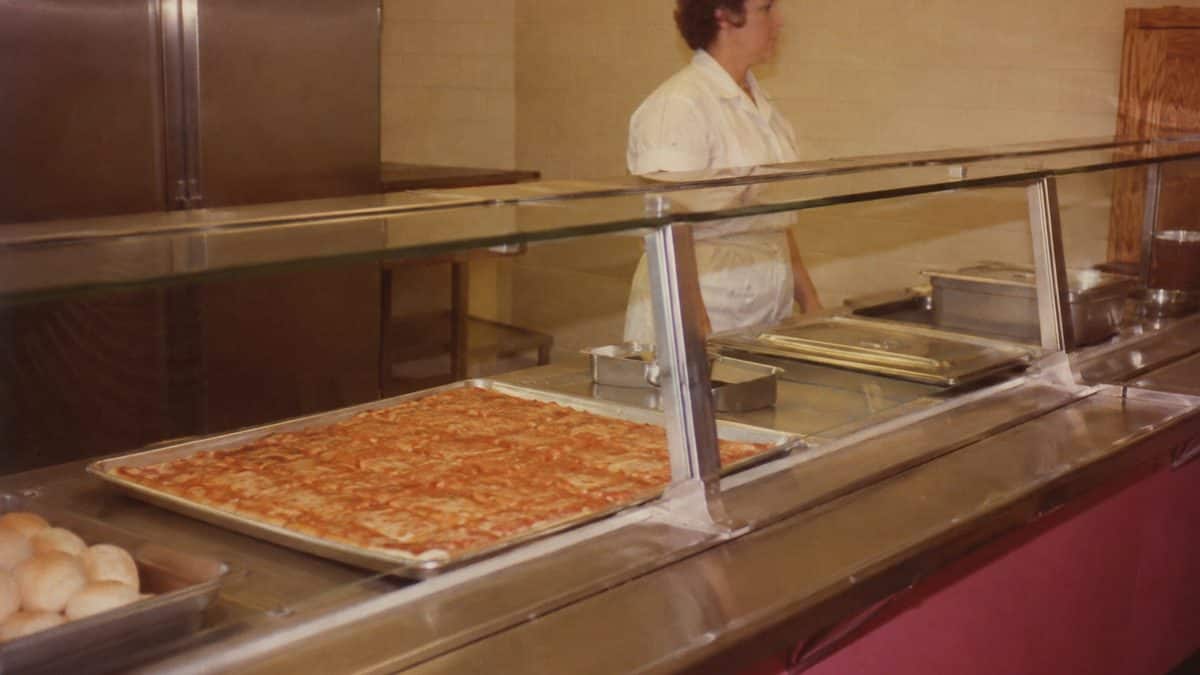 School Cafeteria Food from the '70s We Secretly Loved 2 Genuine vintage-style photo of a 1970s school cafeteria serving line with rectangular pizza.