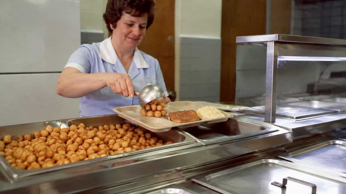 School Cafeteria Food from the '70s We Secretly Loved 6 Realistic vintage photo of tater tots being served onto a cafeteria tray.