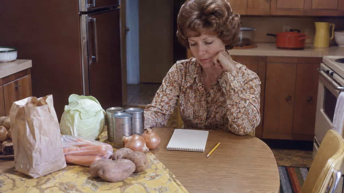 12 Basic Life Skills We Learned in Home Economics That Kids Don't Learn Today 3 Person writing a grocery list at a kitchen table.