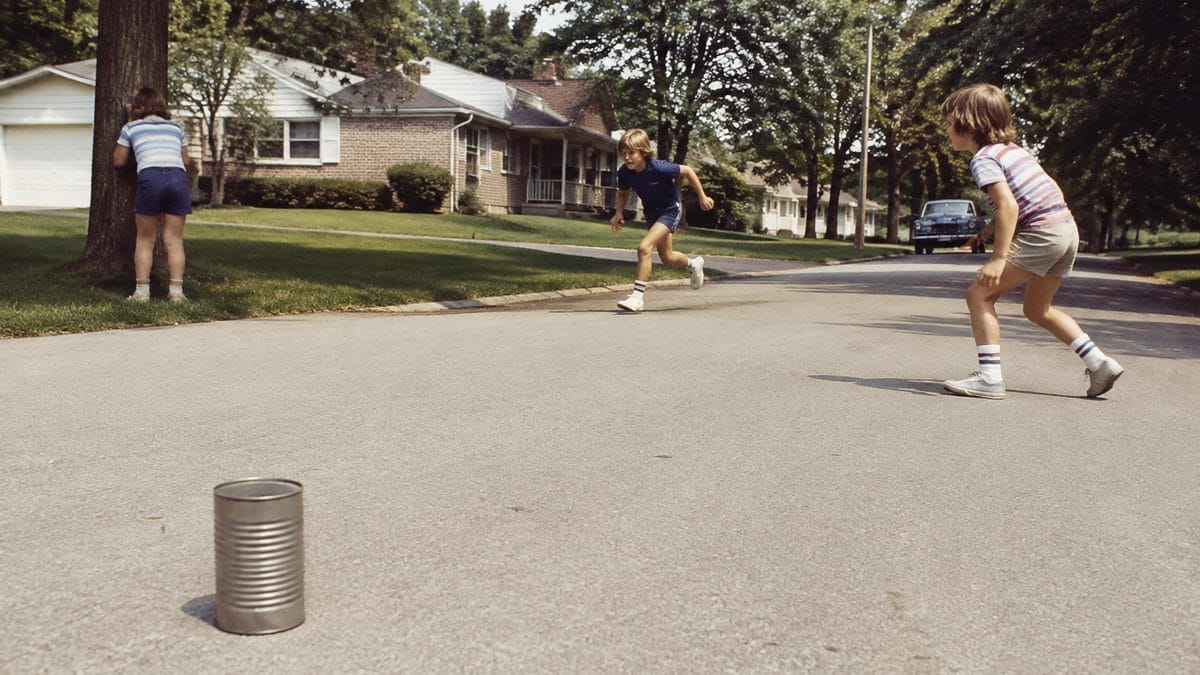 Backyard Games from the '70s That Kept Kids Outside Until Dark 5 Children playing kick the can in a neighborhood.