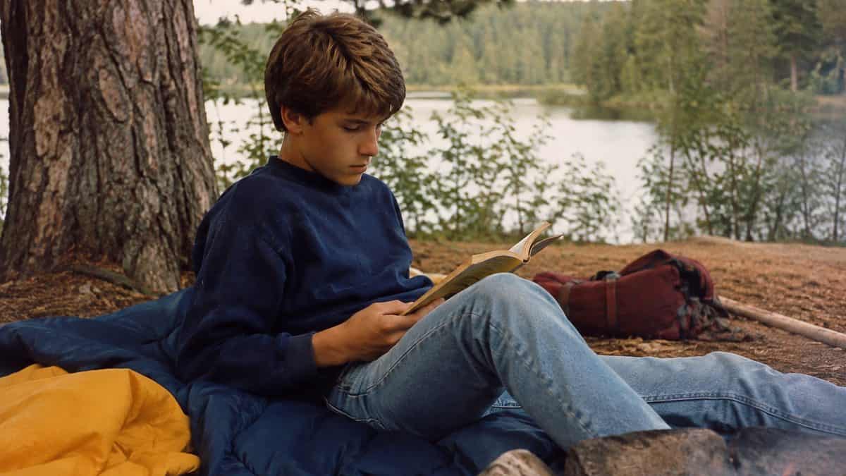 Authentic 1980s photo of a teenager camping or reading outdoors.