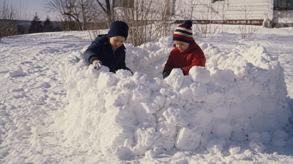 Kids building a snow fort with irregular snow clumps.
