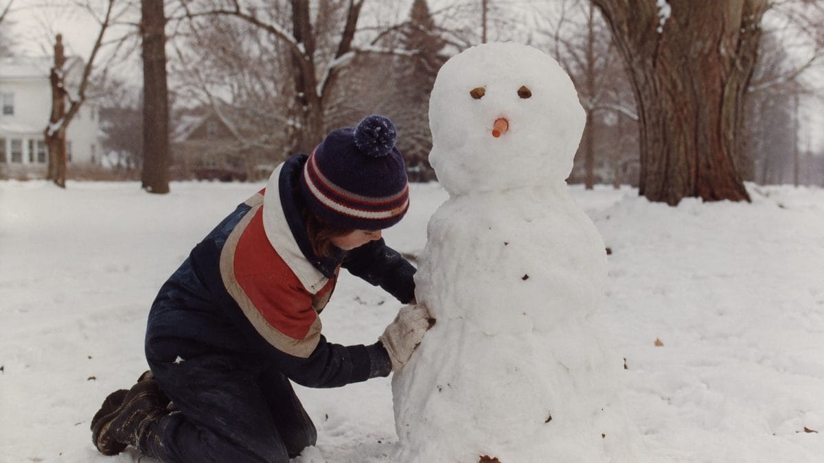Child building a snowman with natural, imperfect details.