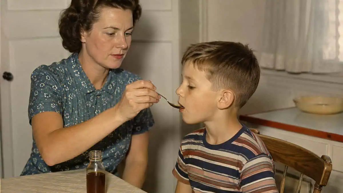 Home Remedies from the '50s Your Grandma Swore By 3 Vintage photo of a mother gently giving medicine to a child with neutral expressions.
