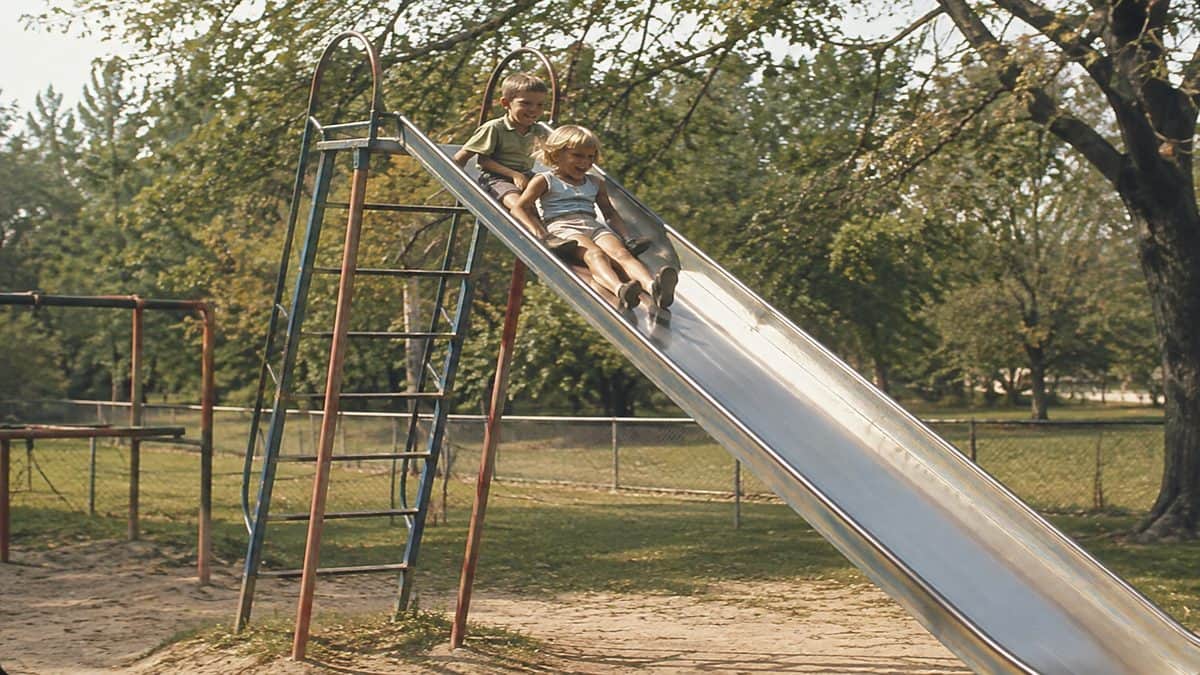 Remember These? 15 Playground Equipment Pieces That Would Never Pass Safety Standards Today 2 Kids on a metal slide.
