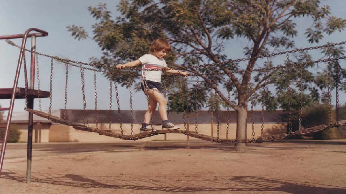 Remember These? 15 Playground Equipment Pieces That Would Never Pass Safety Standards Today 11 Vintage photo of a child playing on a chain bridge playground structure.
