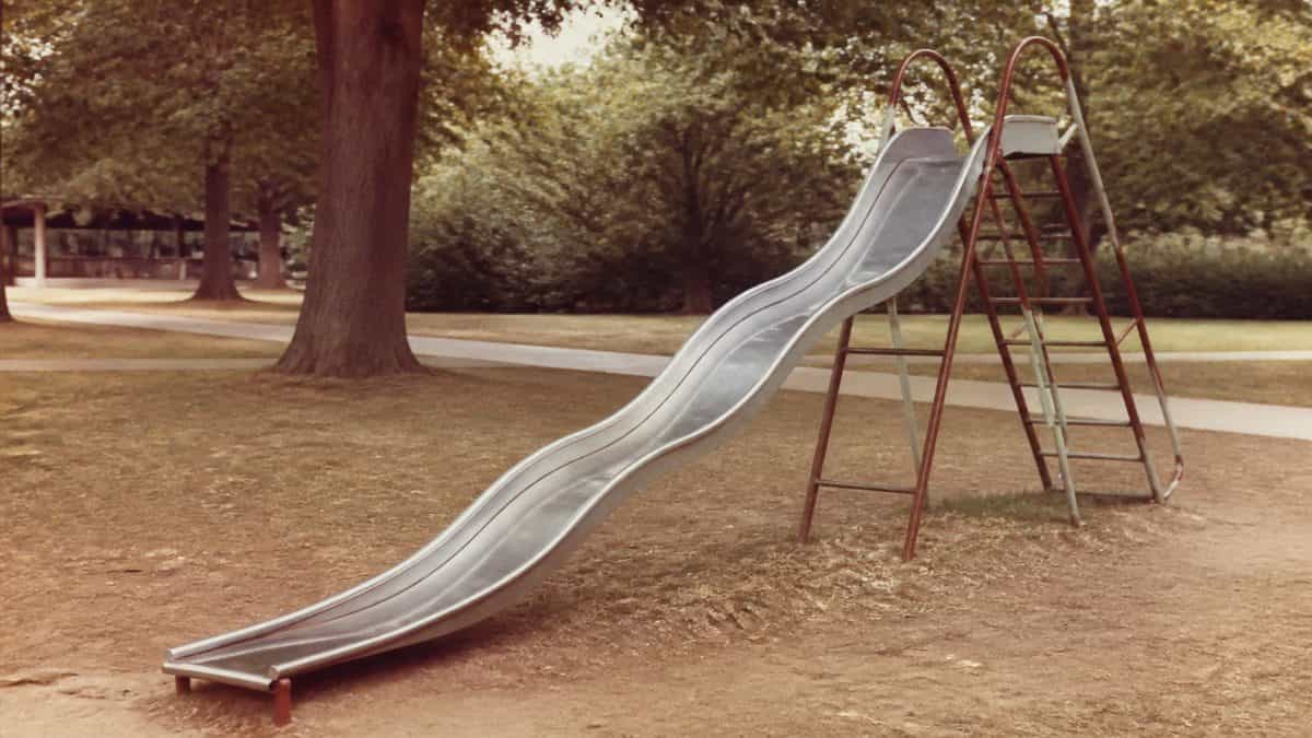 Remember These? 15 Playground Equipment Pieces That Would Never Pass Safety Standards Today 12 Vintage photo of a classic metal wave slide in a park.