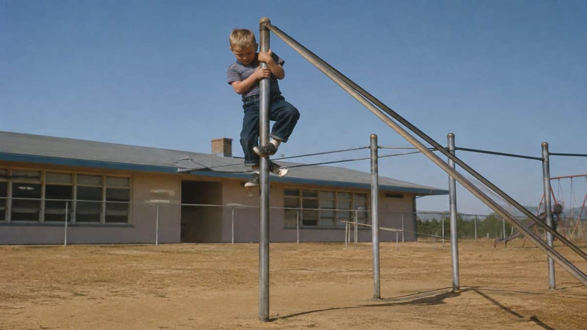 Remember These? 15 Playground Equipment Pieces That Would Never Pass Safety Standards Today 16 Vintage photo of a child climbing a metal pole or jungle gym.