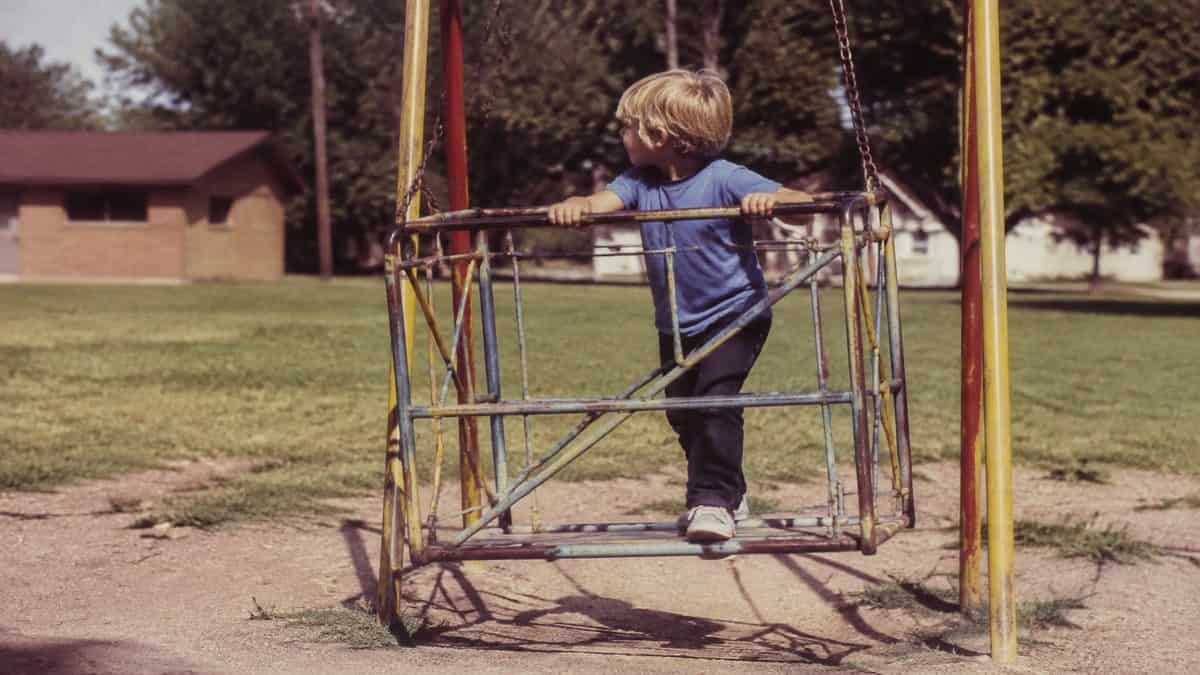 Remember These? 15 Playground Equipment Pieces That Would Never Pass Safety Standards Today 10 Genuine photo of a child playing on a playground swinging gate or similar vintage equipment.