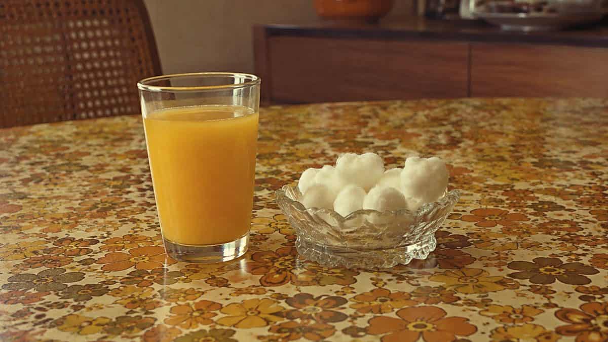 Glass of juice and cotton balls on a retro table.