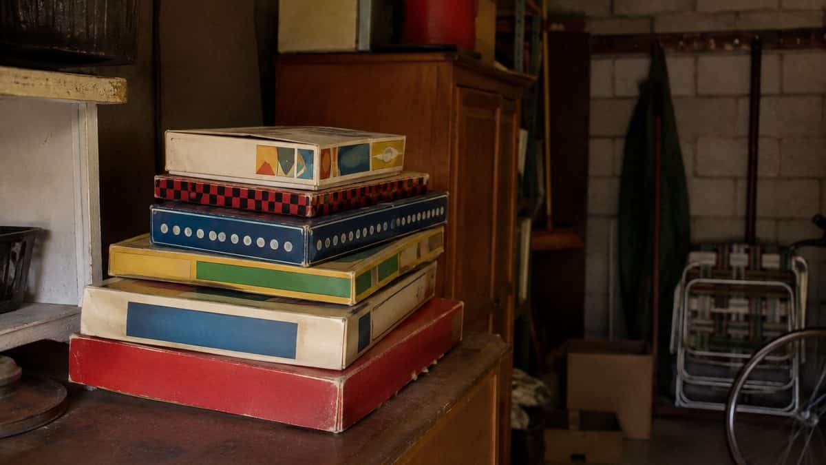 Real photograph of classic vintage board game boxes stacked in a garage.