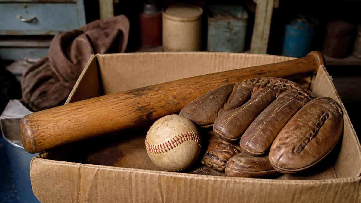 Real photo of an old baseball glove, bat, and ball in a dusty garage box.