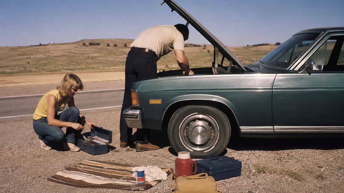 Family fixing a car on the side of the road.