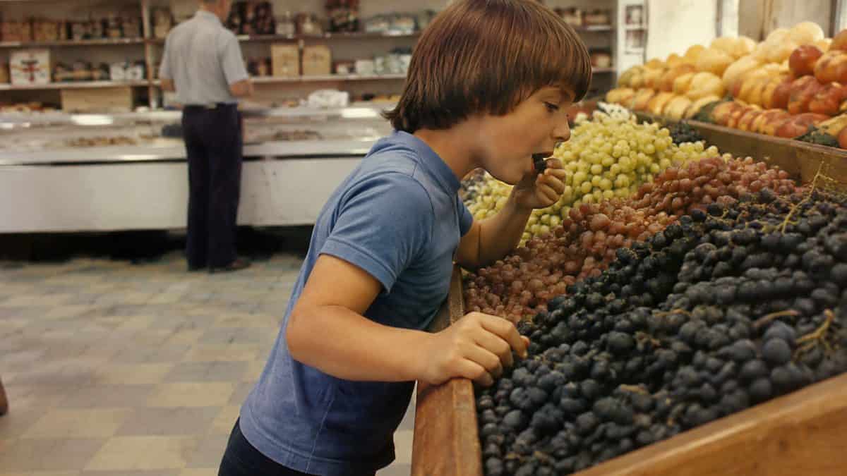 What Kids Used to Do at the Grocery Store That's Unthinkable Now 4 Child sneaking a grape from a realistically sized and rendered bunch of produce