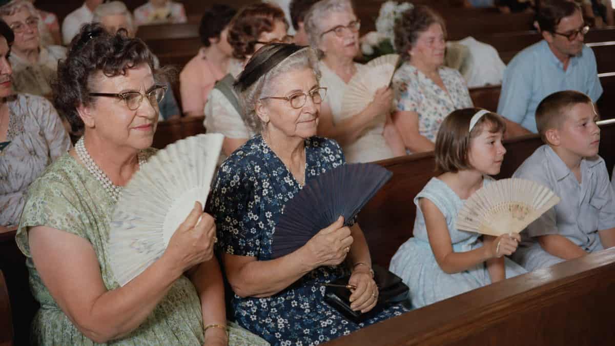 People using paper fans in a church or hot room