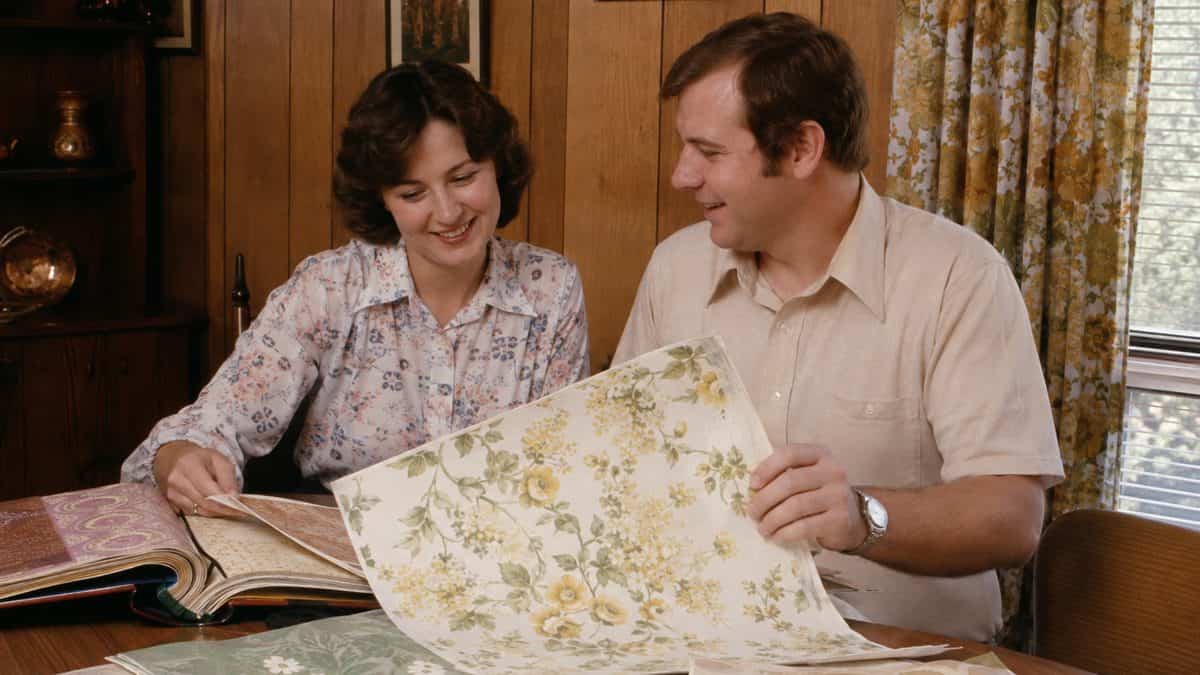 14 Things Every Kid With Wood-Paneled Walls Remembers 2 Real photograph of a couple happily looking at vintage wallpaper samples together.